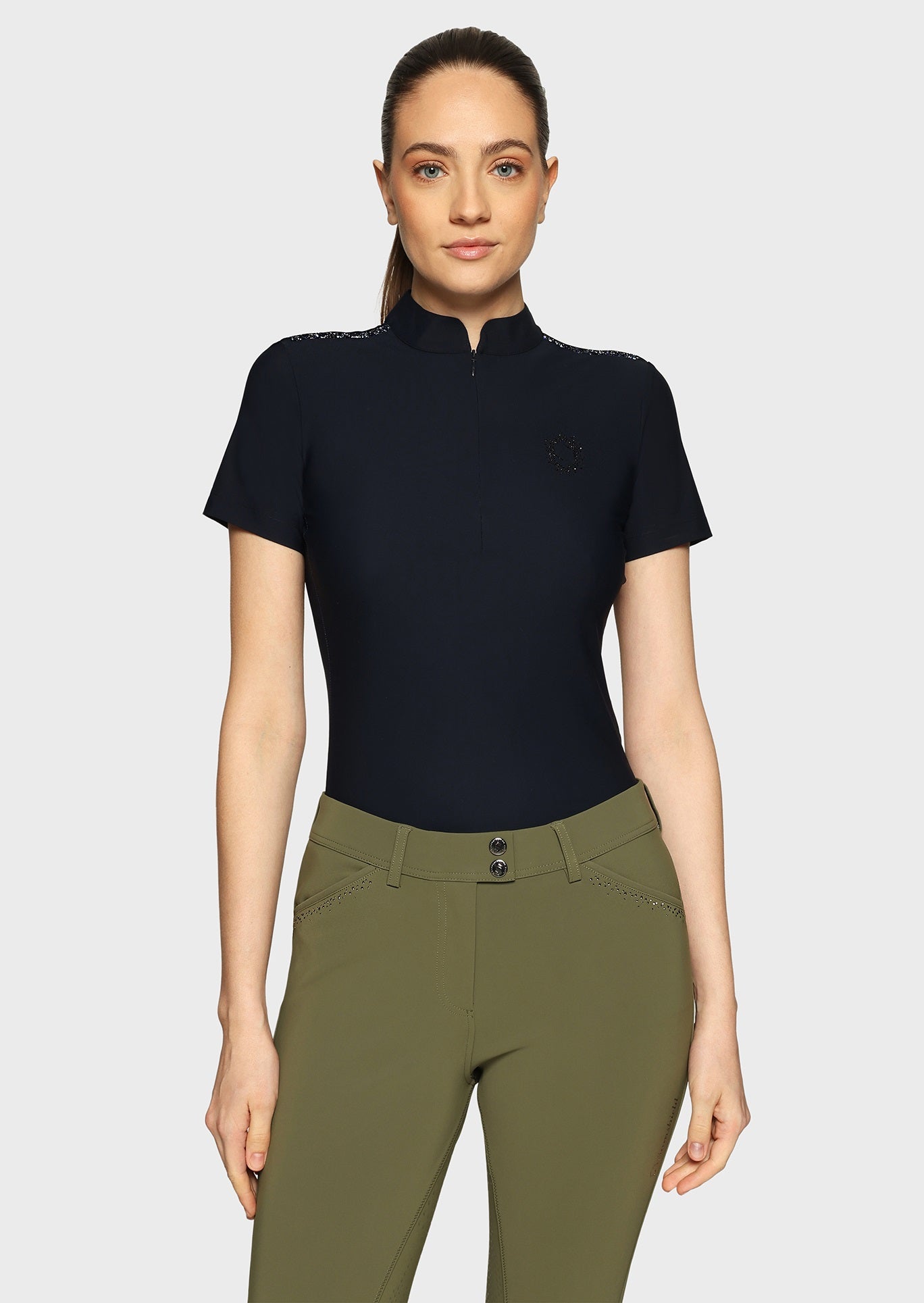 Woman wearing a navy top and olive breeches on a beige background