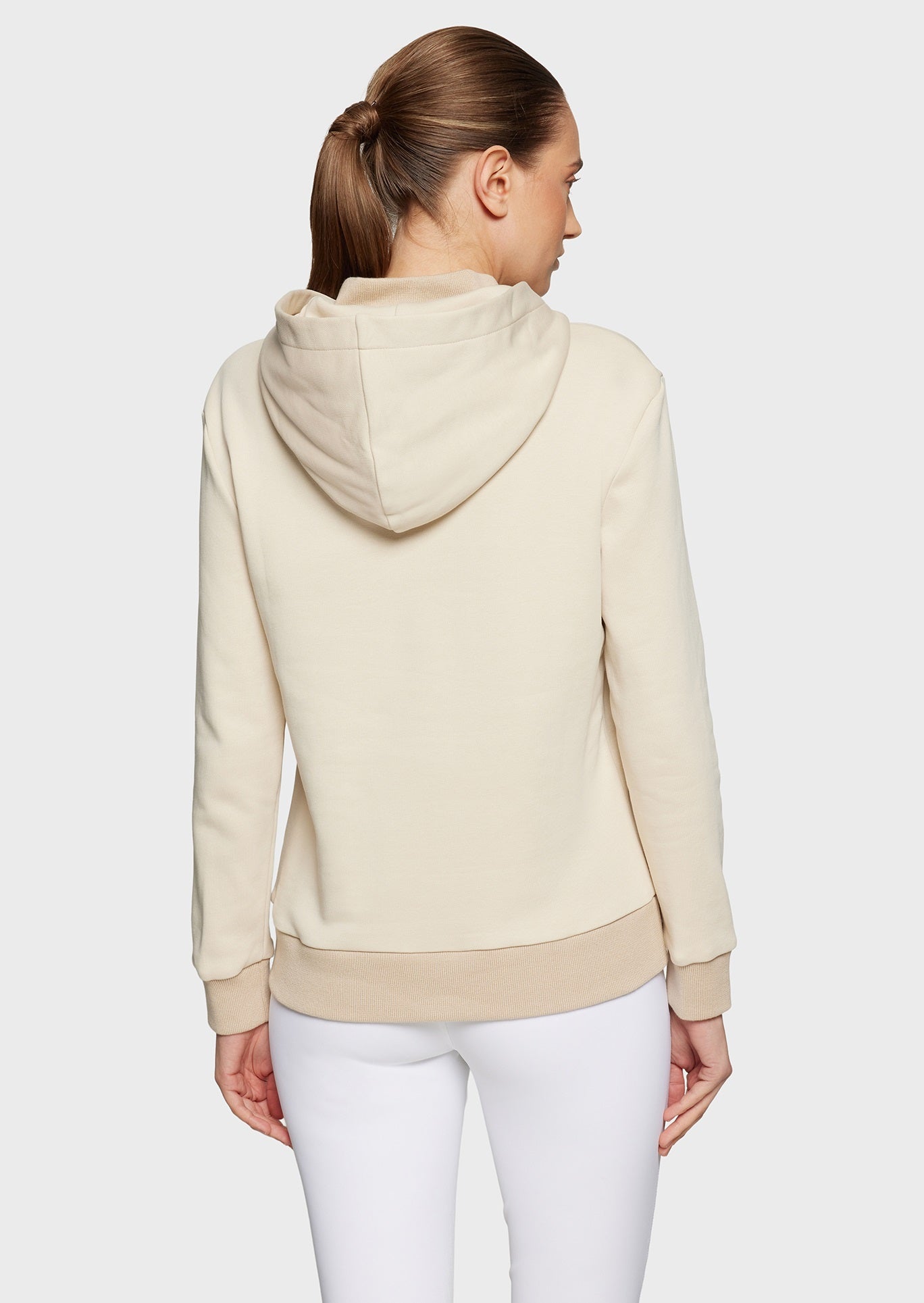 Woman wearing a beige sweatshirt and white breeches on a beige background