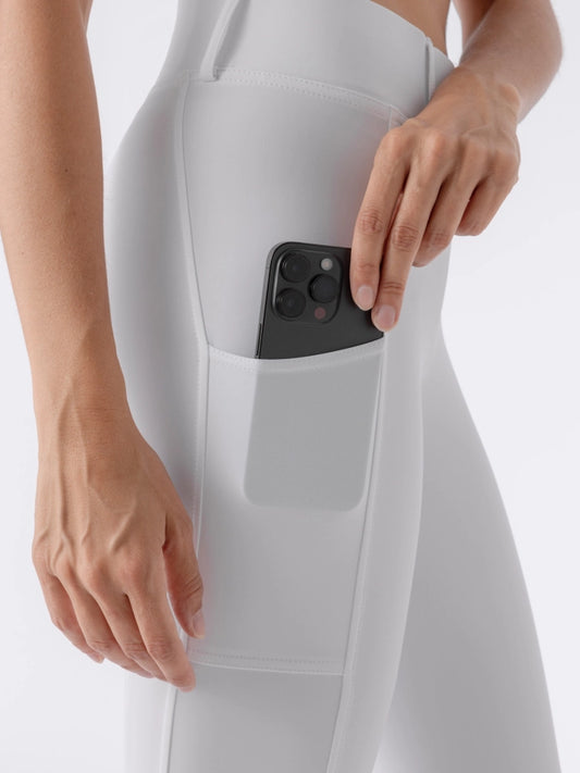 Person wearing a white outfit with a phone in a pocket on a light gray background