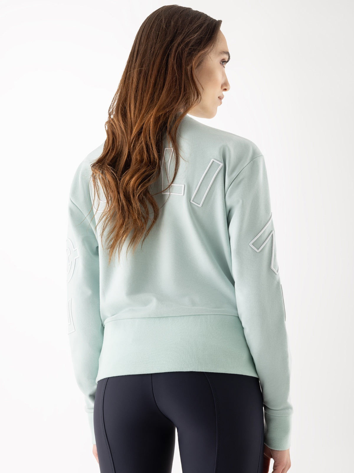 Woman wearing a light green sweatshirt with white accents on a white background