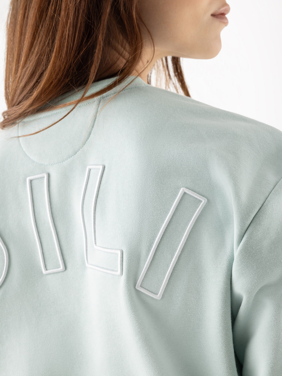 Light green sweatshirt with brand logo on the back, worn by a person.