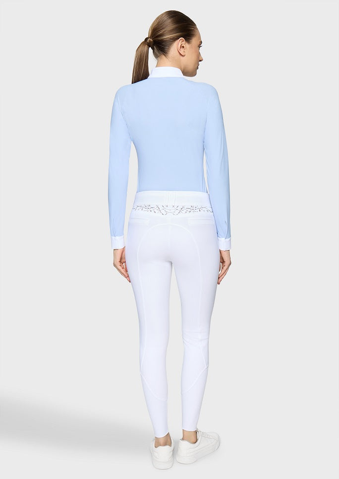 A woman shown from the back wearing a light blue long-sleeve mock-neck top, white leggings with a decorative lace waistband, and white sneakers against a light gray studio background.