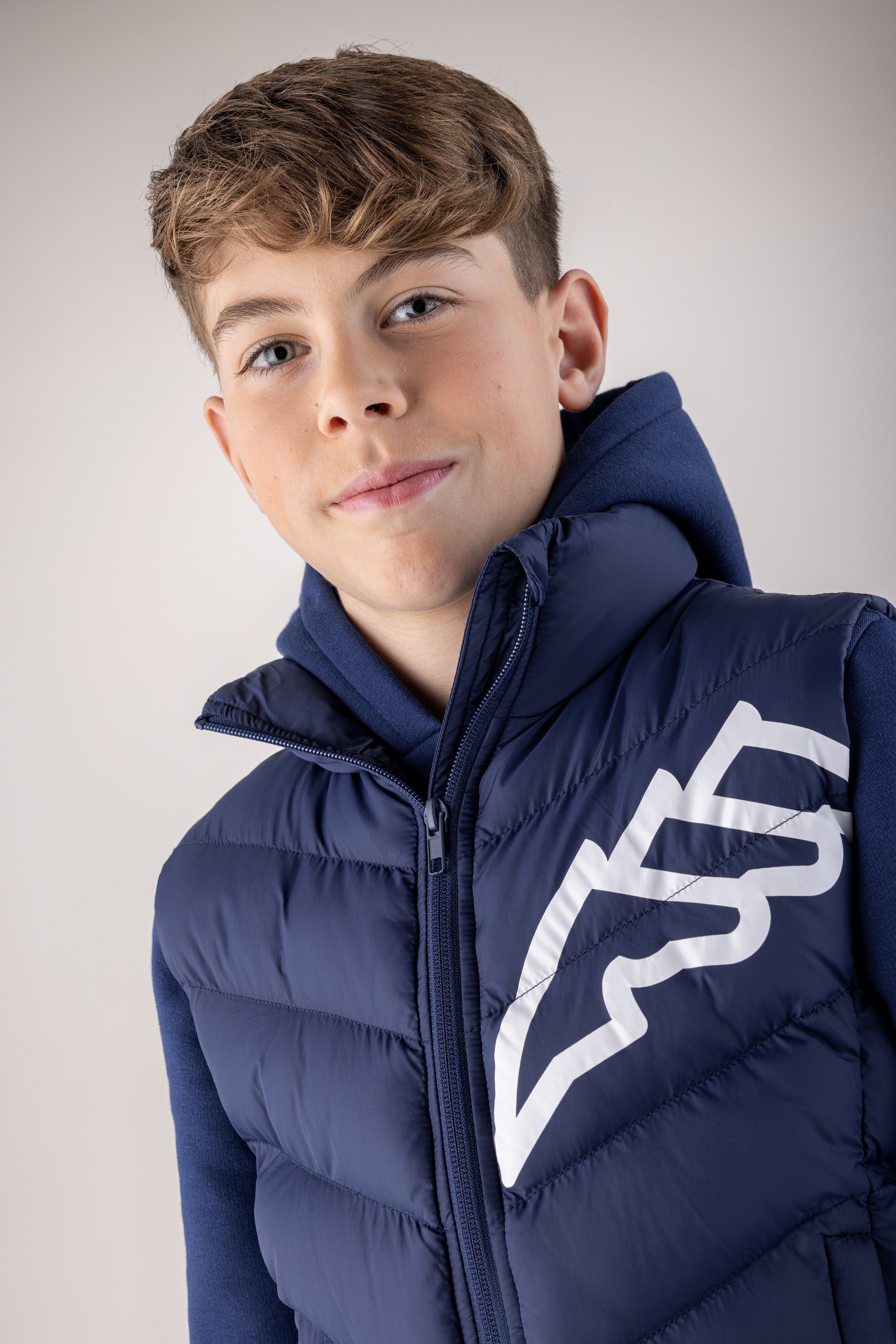 Young boy wearing a navy blue puffer jacket with a white logo on a light gray background