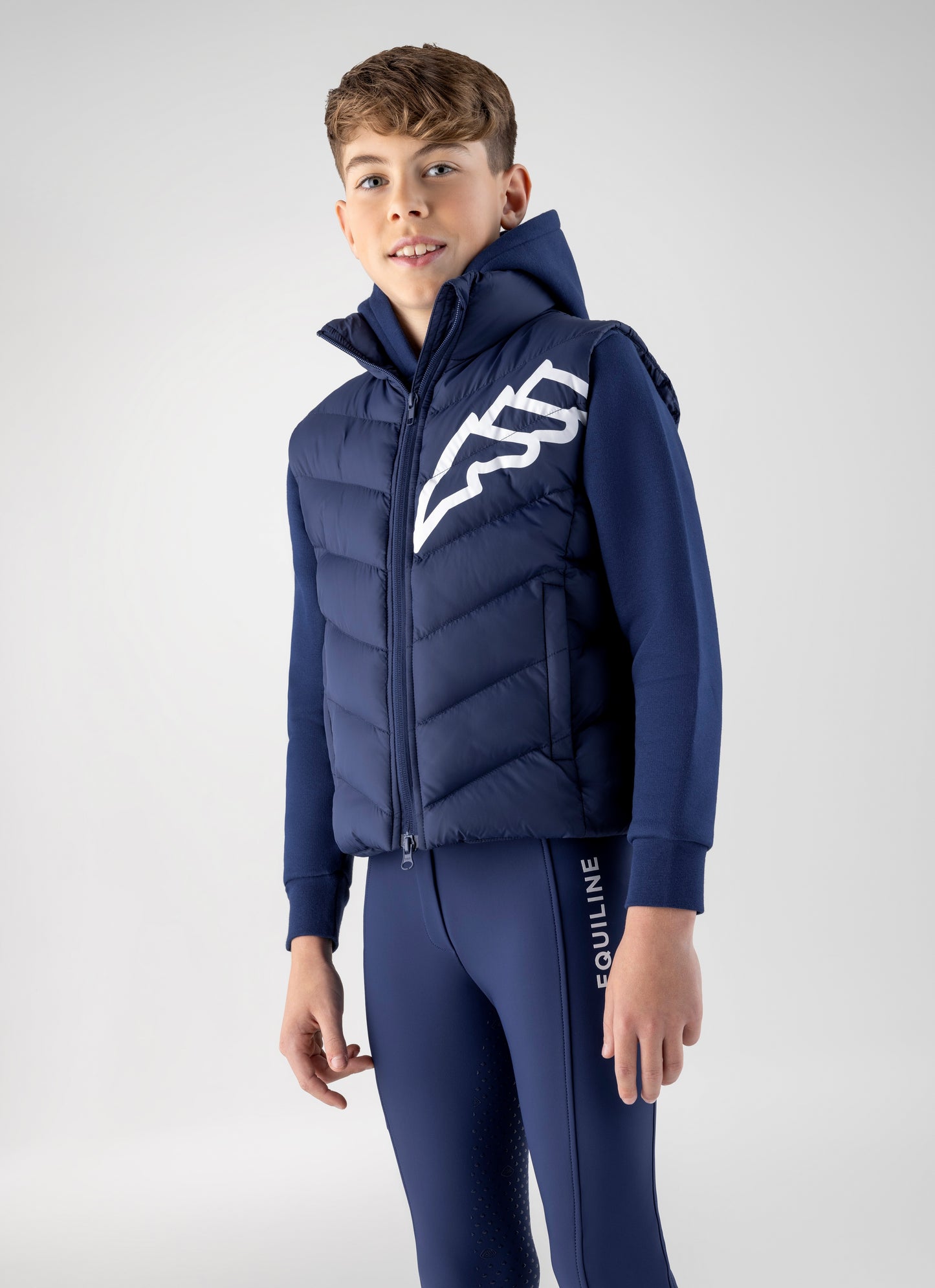 Child wearing a blue puffer vest with a logo and matching pants on a light gray background