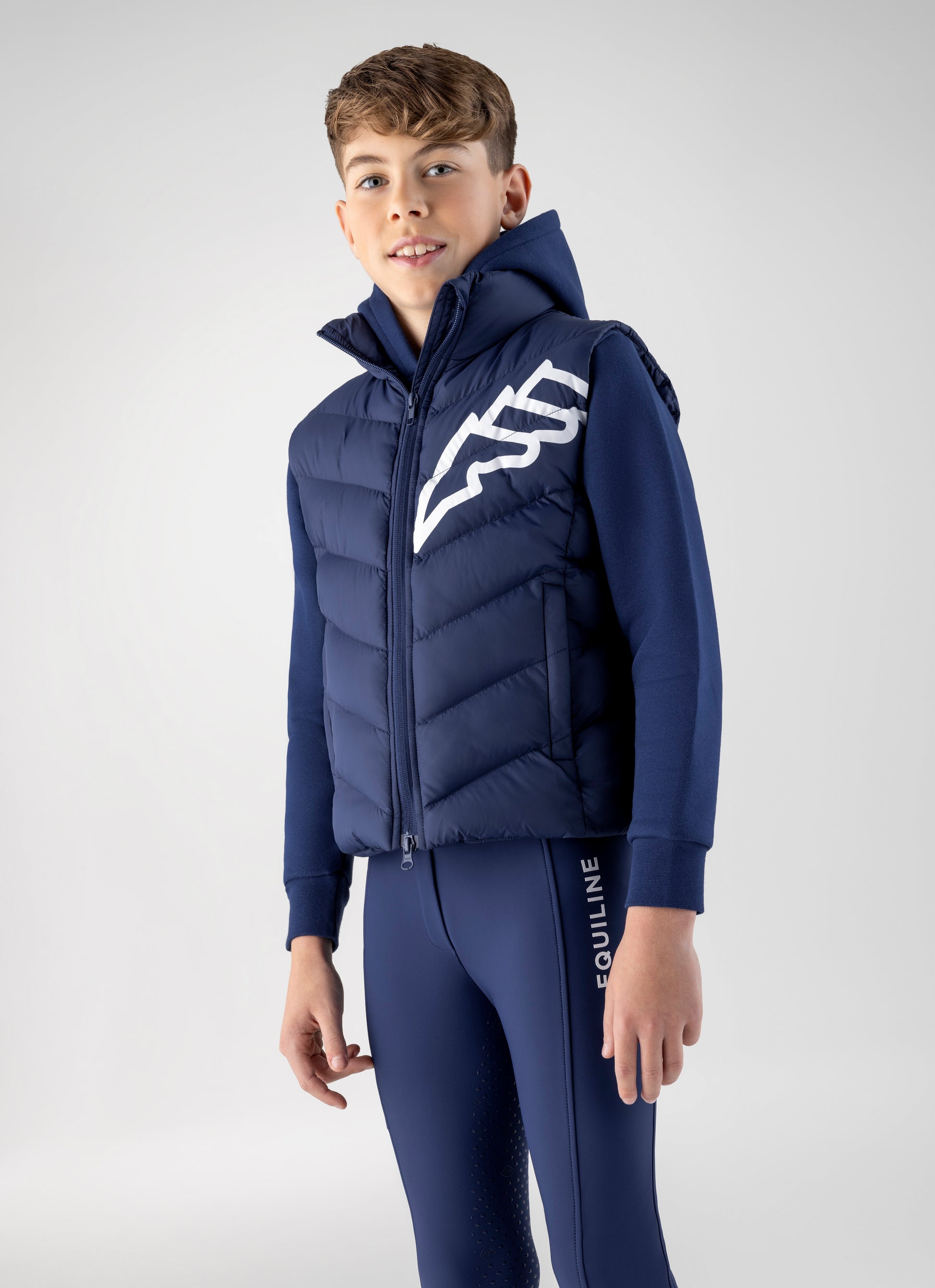 Child wearing a blue puffer vest with a logo and matching pants on a light gray background