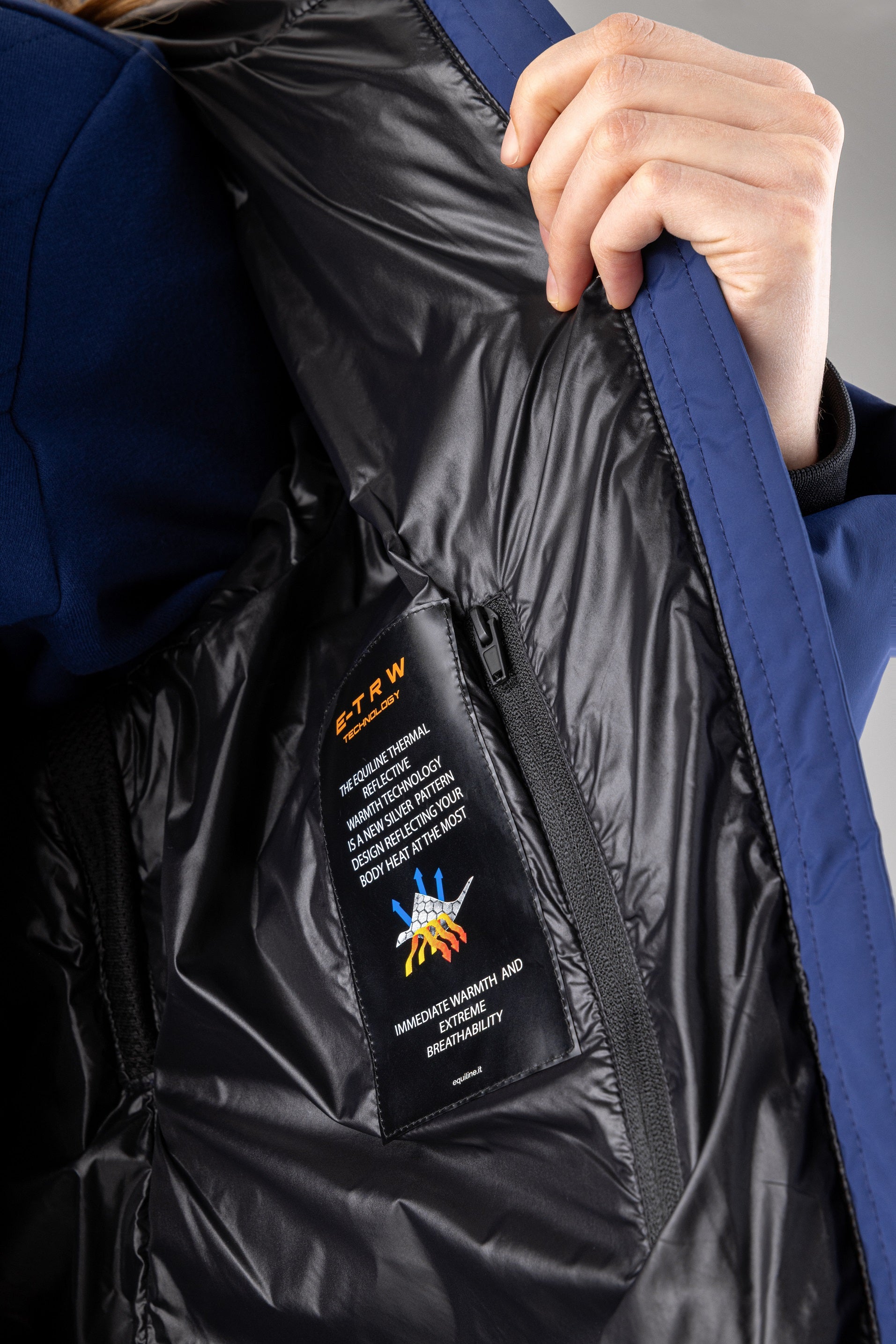 Close-up of a blue jacket with a brand label being held open by a hand.