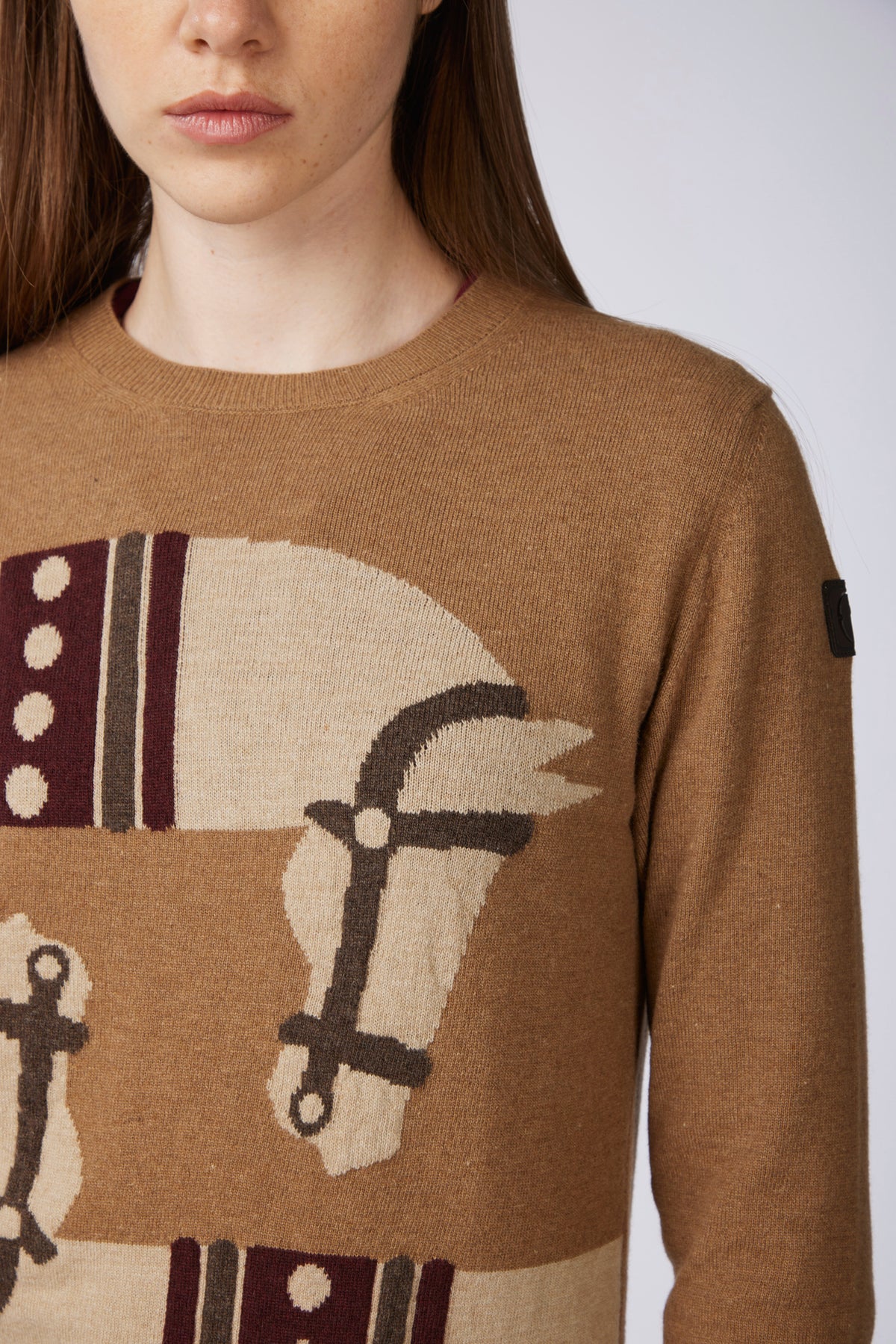 A close-up of a model wearing a brown knit sweater featuring a large horse motif in beige and dark brown.