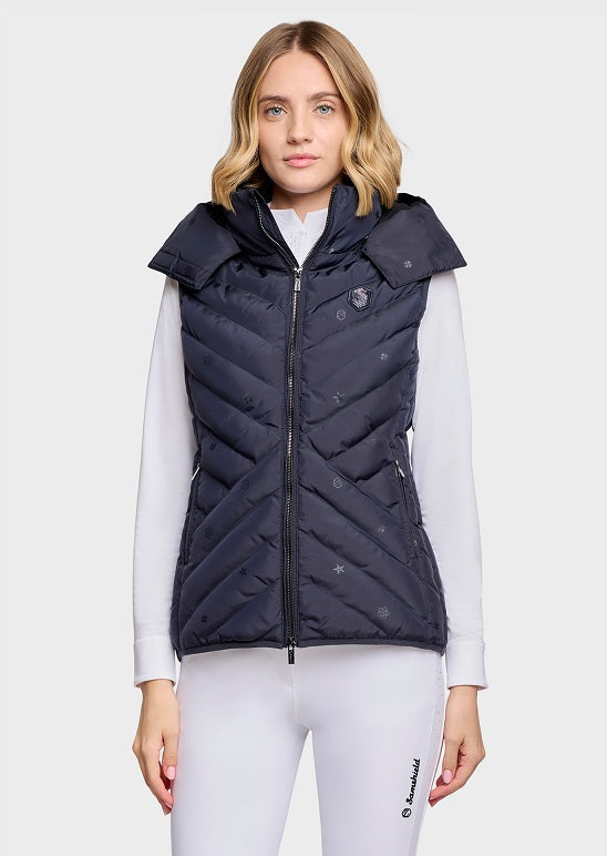 A woman modeling a sleeveless quilted puffer vest in dark navy blue. The vest features a high collar, full front zipper, and subtle tonal logo details.