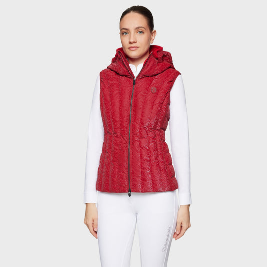 Woman wearing a red puffer vest over a white shirt on a light gray background