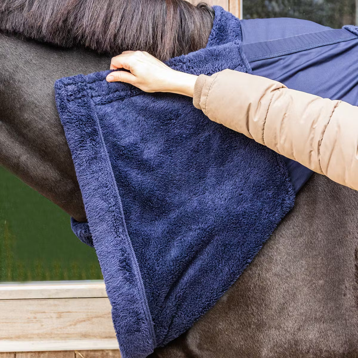 Person adjusting a blue blanket on a horse