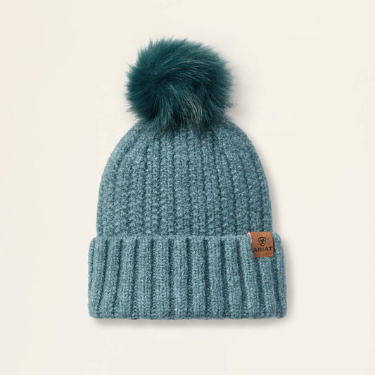 Teal knit beanie with fur pom-pom on a beige background