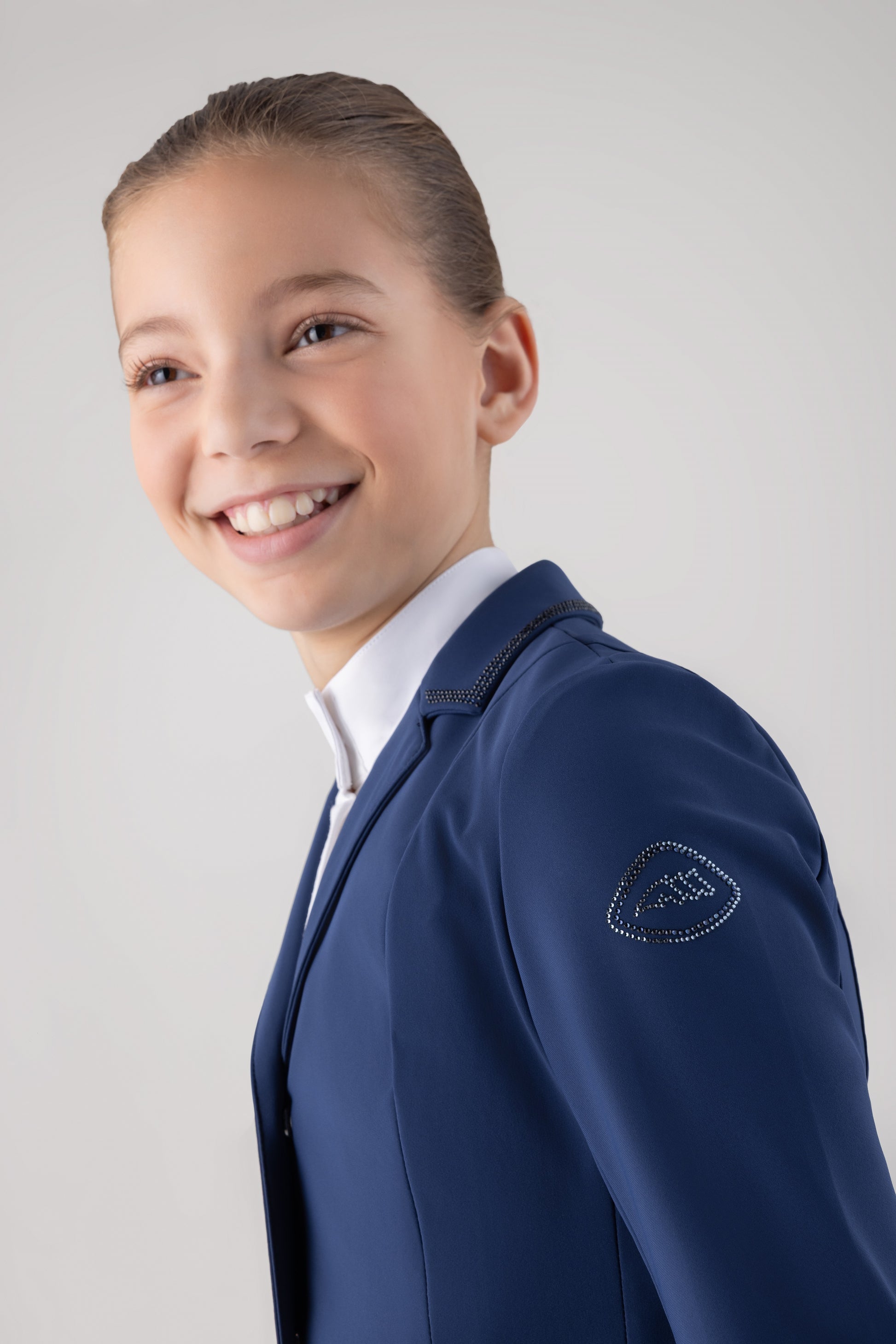 Young girl wearing a blue blazer with a visible brand logo on a light gray background