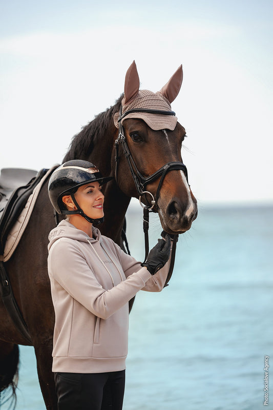 Woman in equestrian gear standing next to a horse by the water