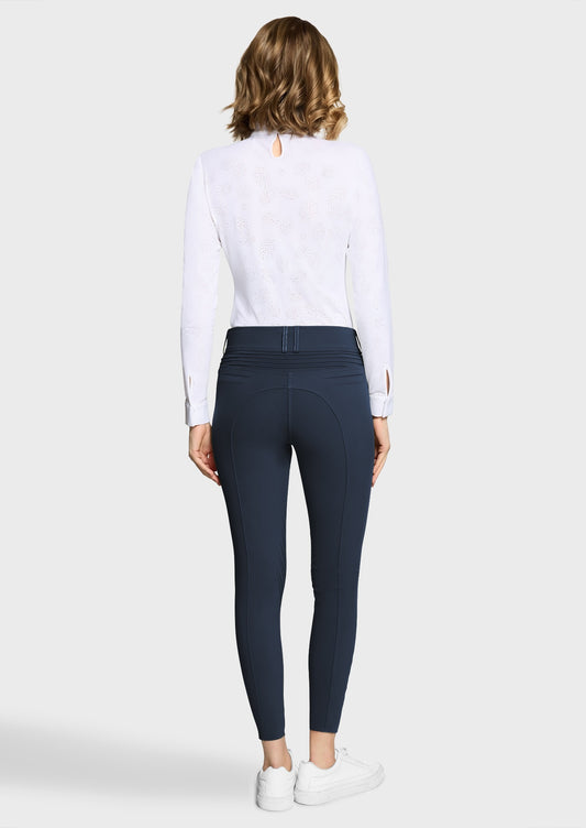 Woman wearing a white competition shirt and navy breeches on a beige background