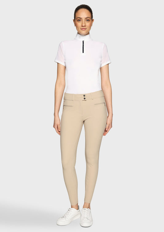Woman wearing a white competition shirt and beige breeches on a beige background