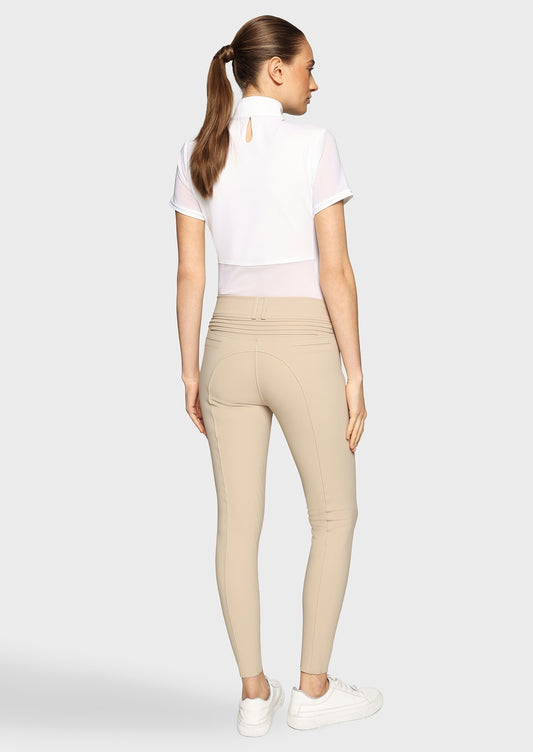 Woman wearing a white competition shirt and beige breeches on a beige background