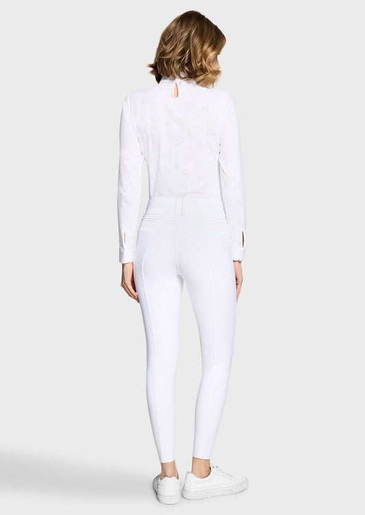 Woman wearing a white competition shirt and white breeches on a beige background