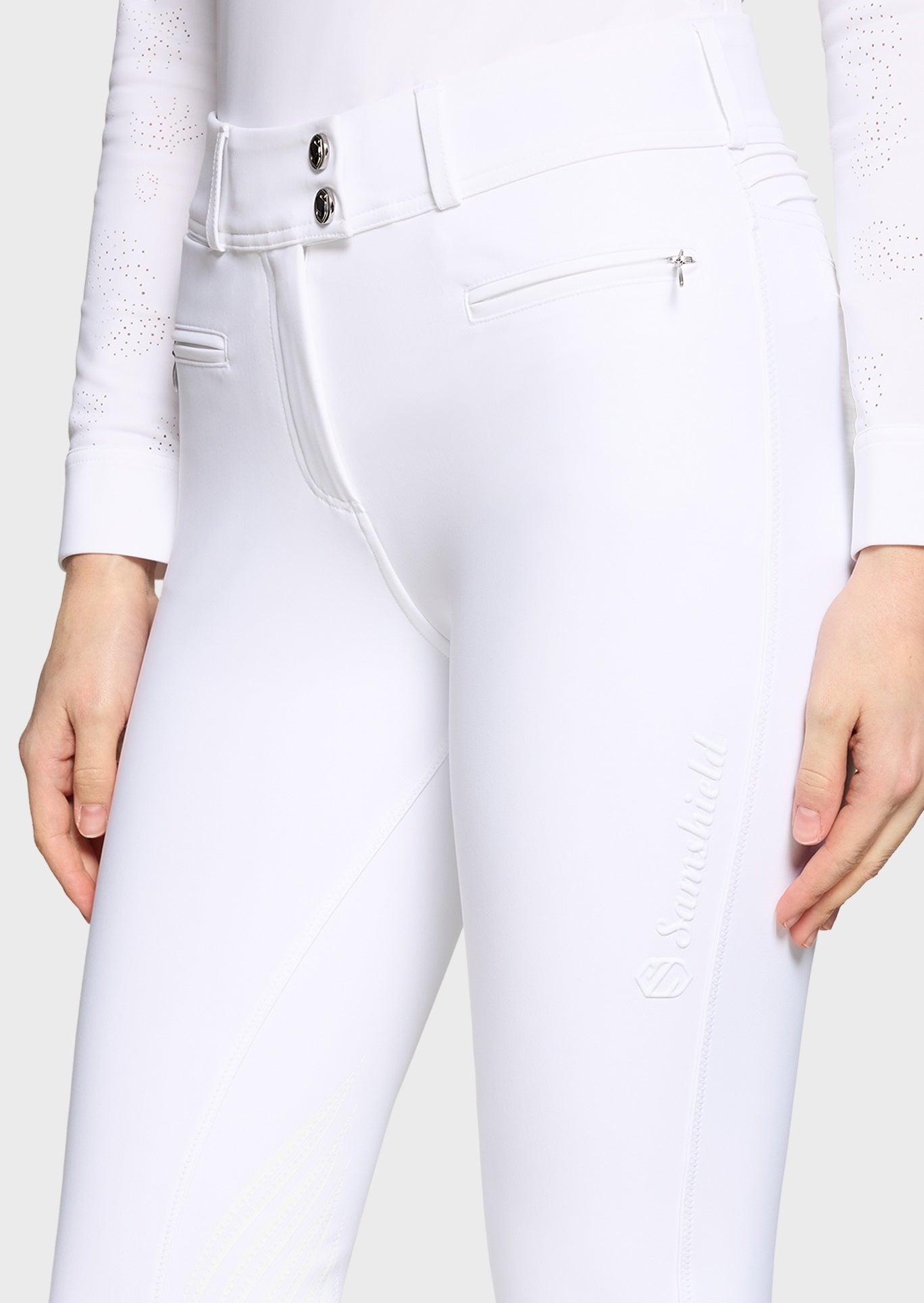 Woman wearing a white competition shirt and white breeches on a beige background