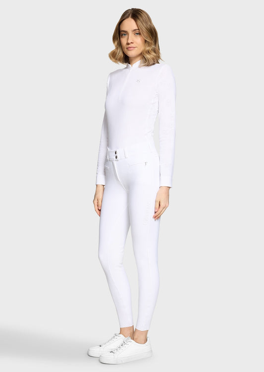 Woman wearing a white competition shirt and white breeches on a beige background