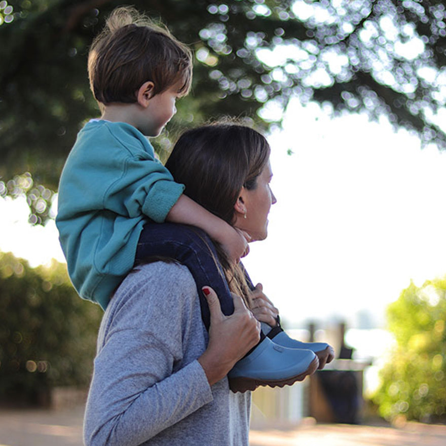 Woman carrying a child on her shoulders outdoors with trees in the background