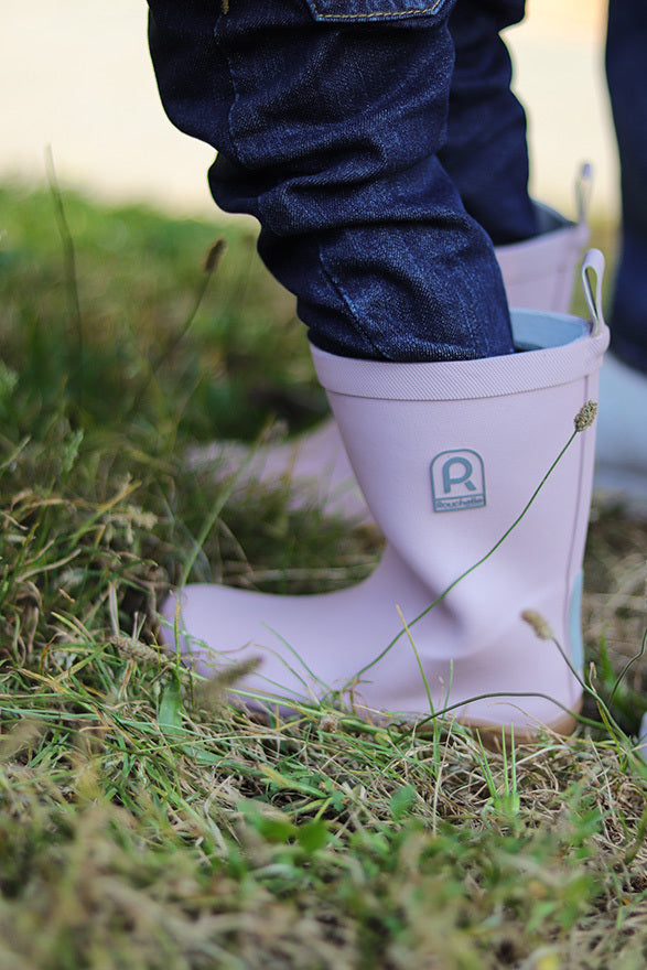 Pink kids wellington boots being worn by a child on grass.