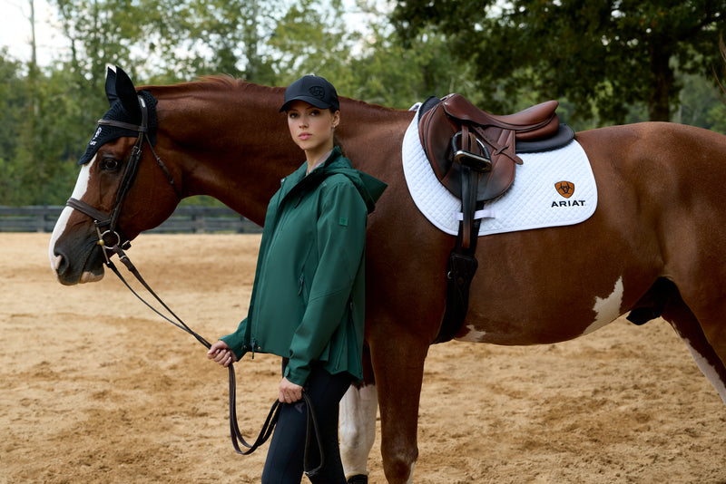Woman in a green coat standing next to a brown horse in an outdoor setting