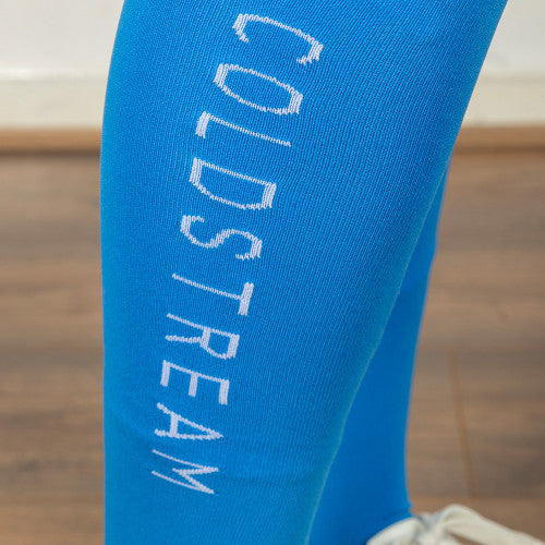 A close-up of a bright blue ribbed sock or leg warmer with the word 'COLDSTREAM' printed vertically in white on the calf, shown against a blurred indoor background.