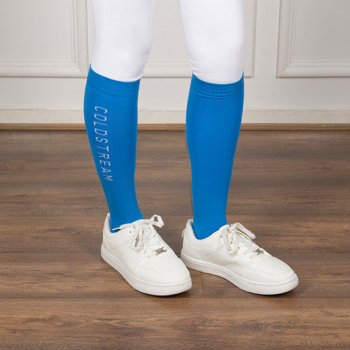 Person wearing blue knee-high socks with 'Coldsream' branding on a wooden floor.