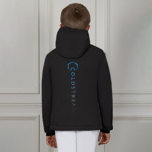 Person wearing a black hoodie with a logo and text on the back, standing against a light-colored paneled wall.