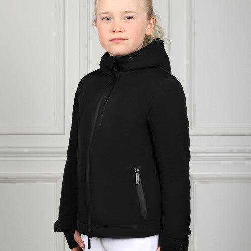Young girl wearing a black jacket against a white paneled wall