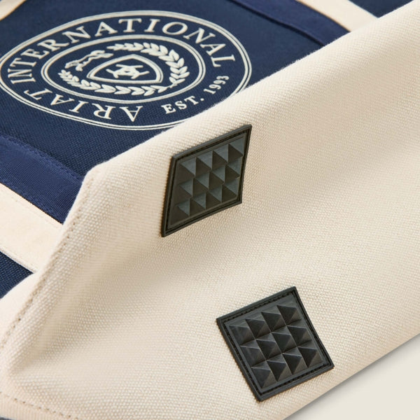 Close-up of a beige bag with black pyramid pattern and 'International Arpia' logo on a blue background.