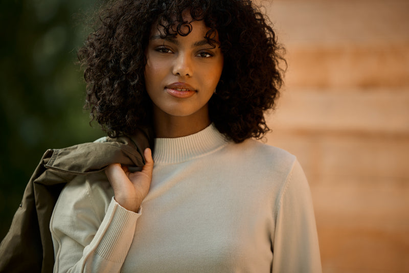 Woman wearing a white jumper holding a green jacket
