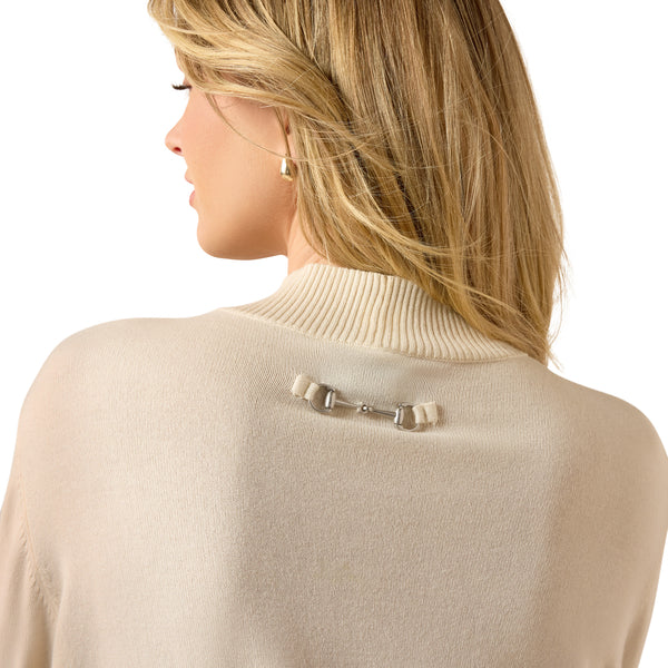 A woman shown from the back wearing a cream-colored ribbed turtleneck sweater with a silver horsebit accessory attached at the base of the neck, against a solid white background.
