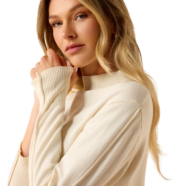 A woman in a beige sweater holding her hands up to her face on a white background