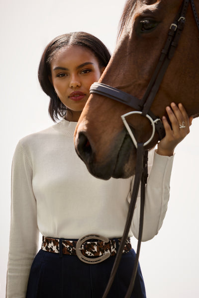 A woman in a white sweater and navy skirt holding a bay horse