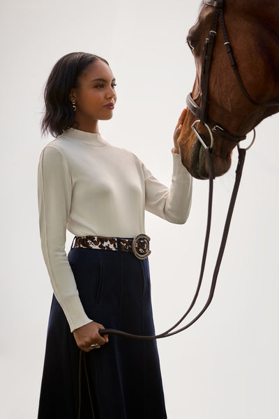 A woman in a white sweater and navy skirt holding a bay horse