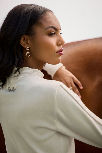 A woman wearing a cream sweater with a horse's back in the background