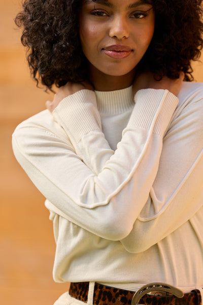 Woman wearing a white jumper with her arms wrapped around her