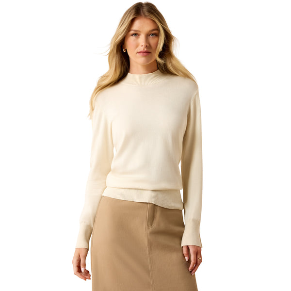 A woman modeling a cream-colored long-sleeve knit sweater with a ribbed mock neck, cuffs, and hem, paired with a beige skirt, against a solid white background.