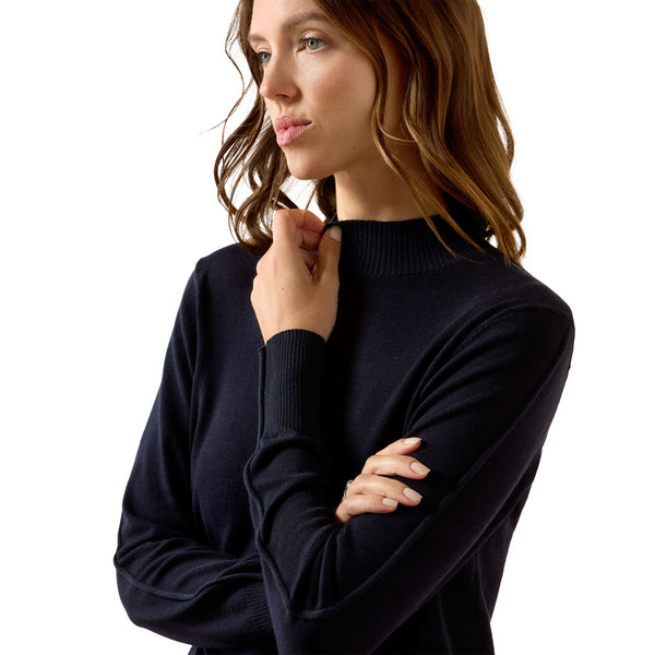 A woman wearing a dark navy ribbed mock neck sweater, shown from the chest up against a solid white background.
