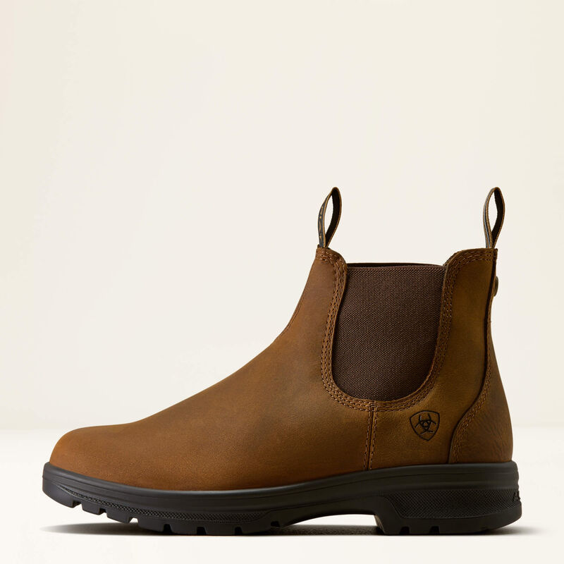 A brown leather Chelsea-style boot with a black sole and heel pull tabs, shown in profile against a light beige background. The brand logo is visible on the side.