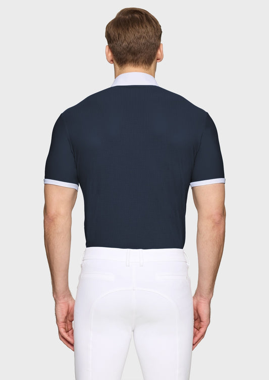 Man wearing a navy competition shirt and white breeches on a beige background