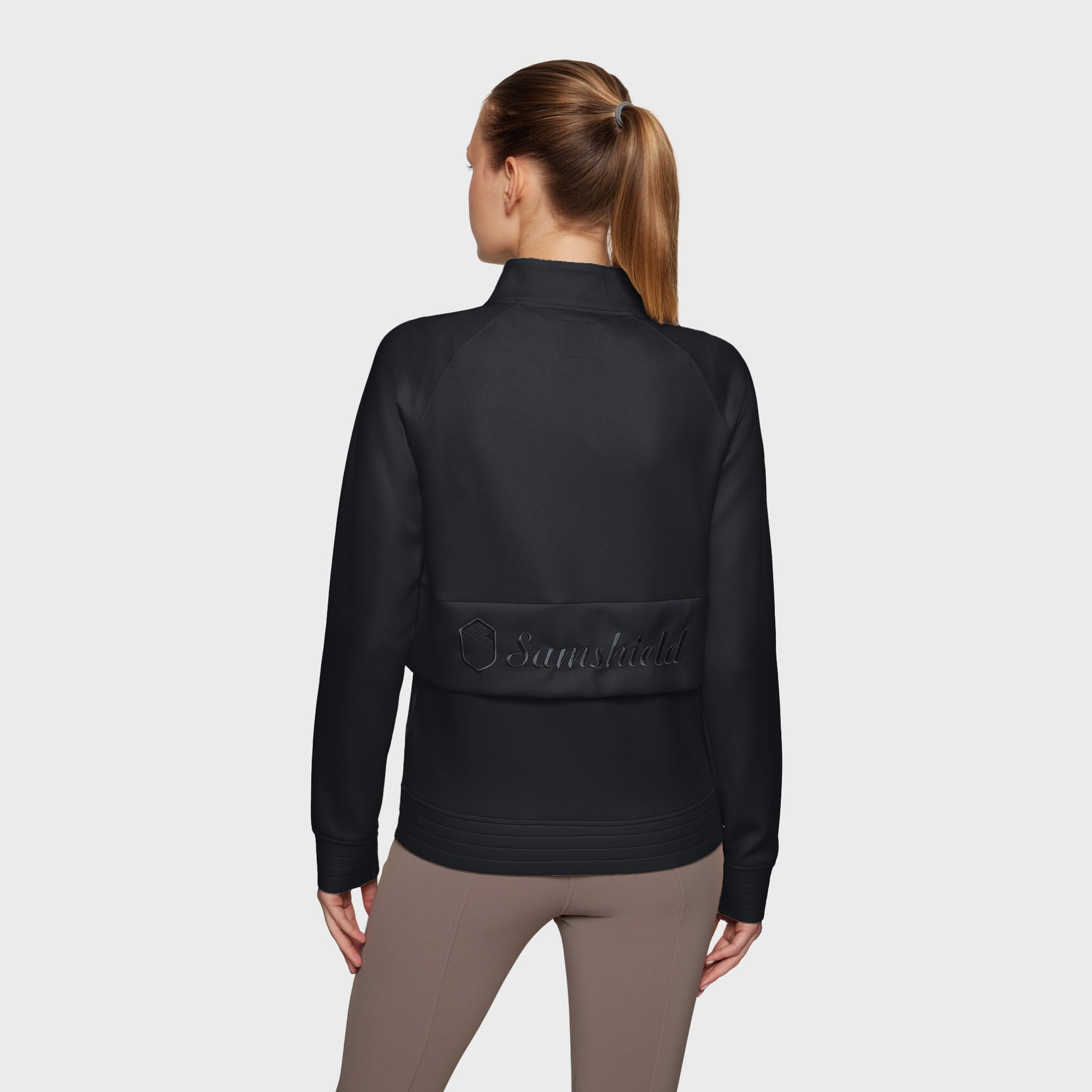 Woman wearing a black jacket with a brand logo on a light gray background