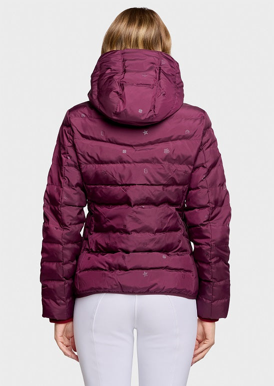 A woman viewed from the back wearing a quilted puffer jacket in deep plum purple with small white embroidered snowflake details, paired with white pants, against a light gray studio background.