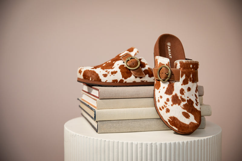 Pair of cow print slip on shoes on top of some books