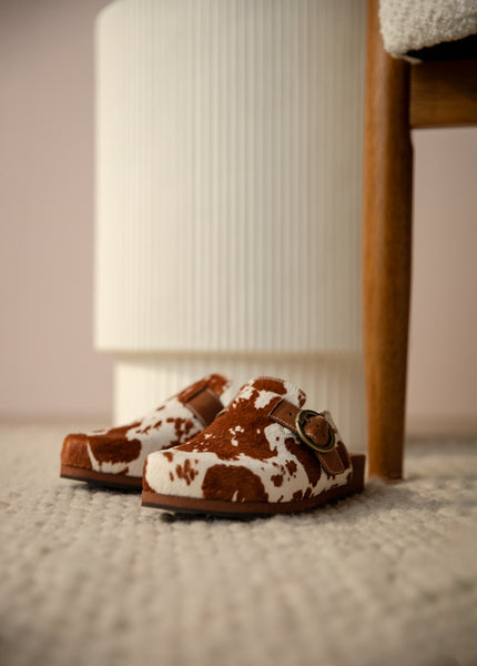 Pair of cow print slip on shoes under a chair leg