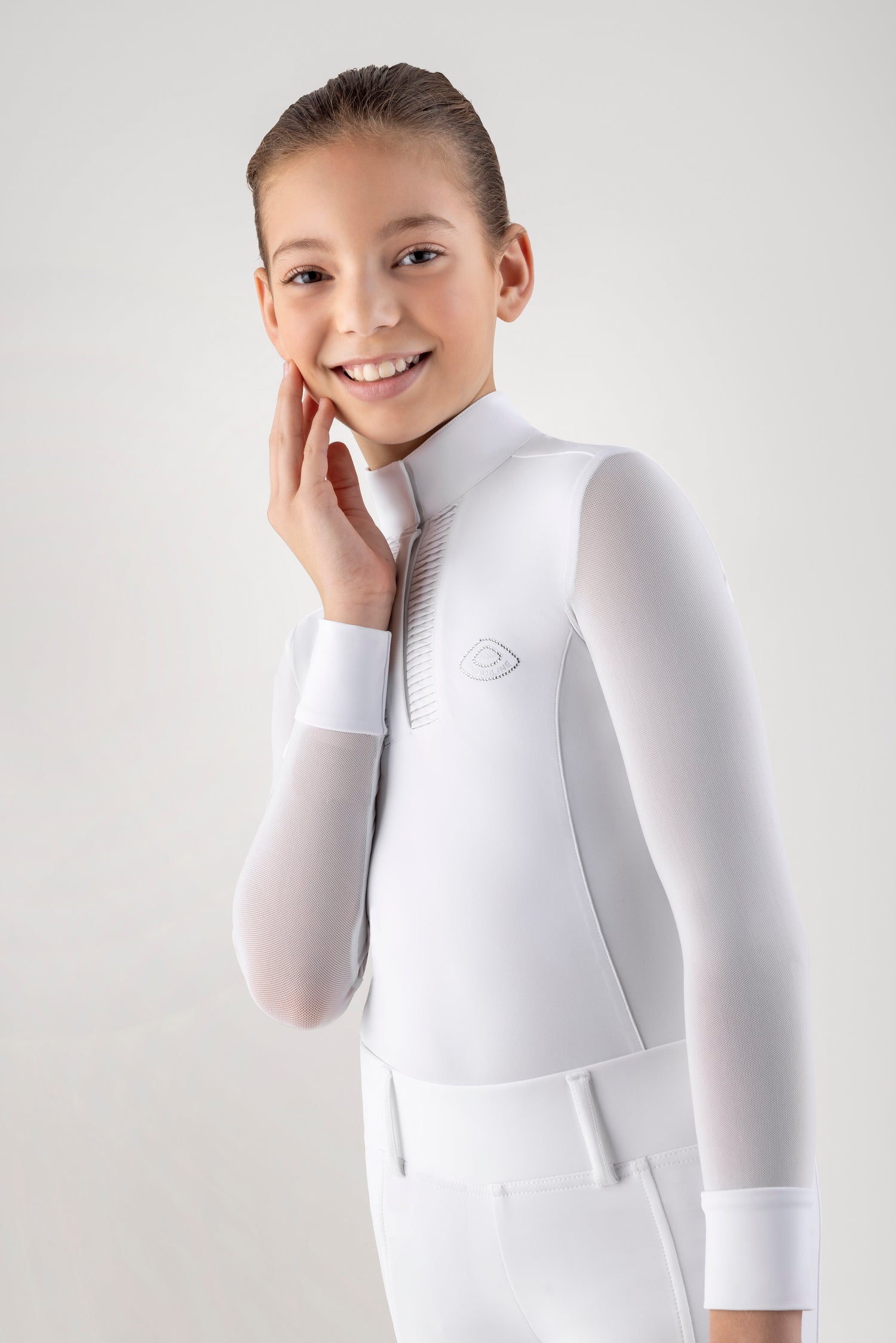 Young girl wearing a white equestrian show shirt and pants on a light gray background