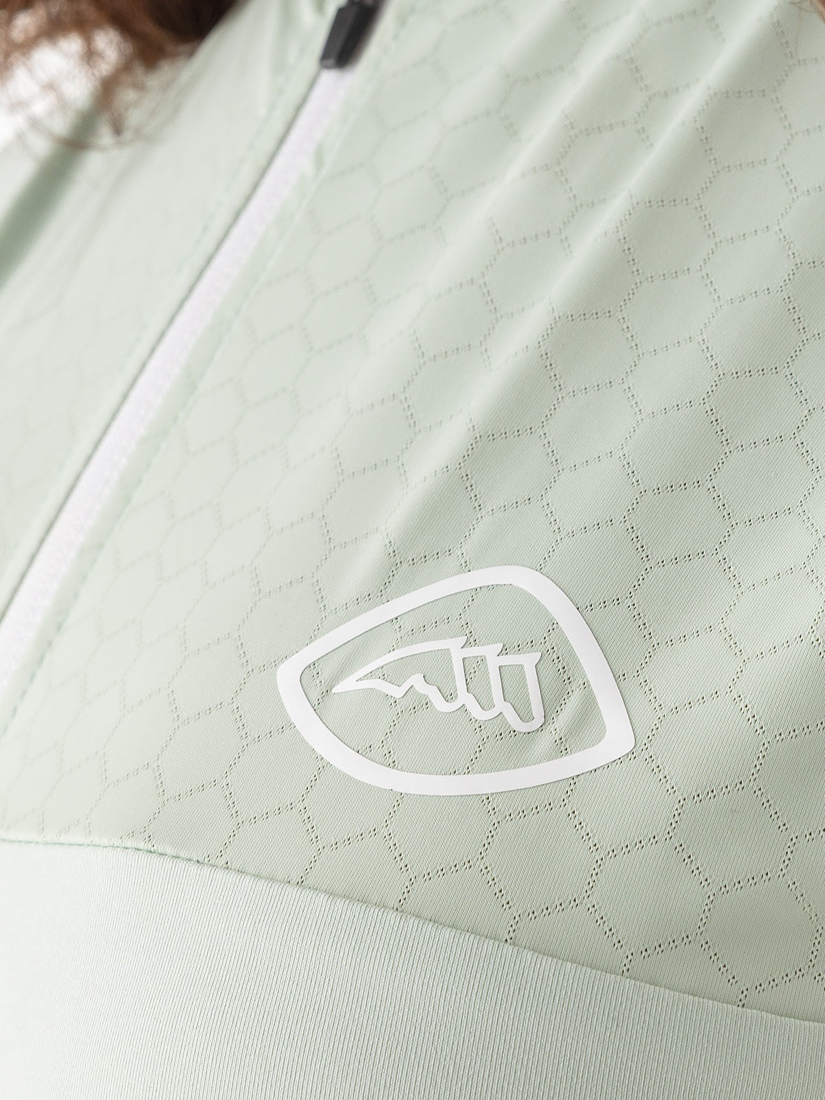 Close-up of a light green quilted top with a brand logo on a matching background