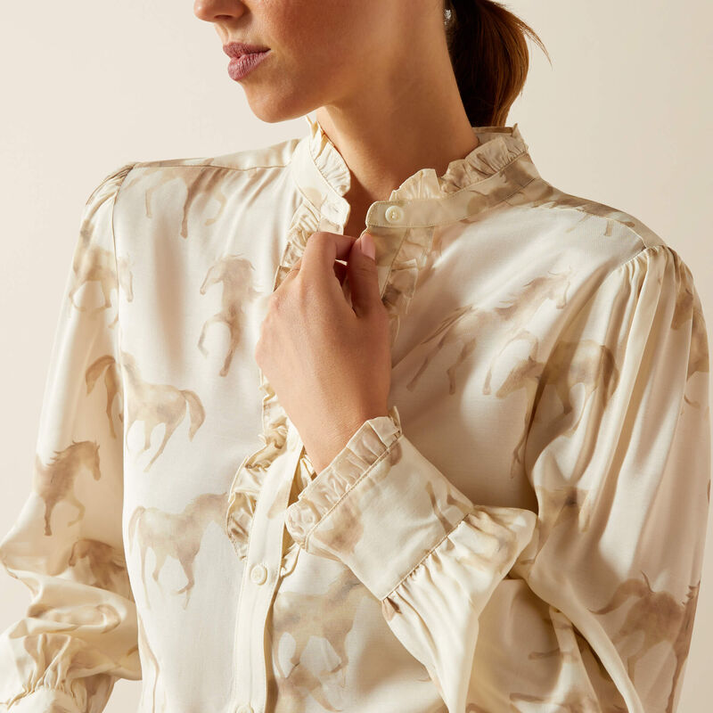Woman wearing a beige horse patterned blouse against a neutral background