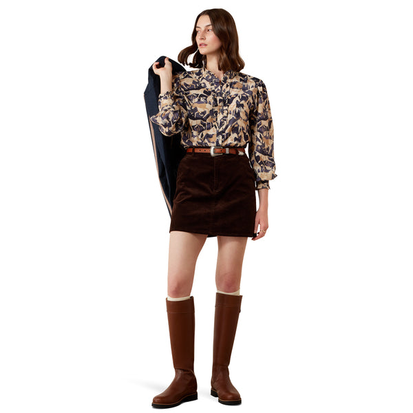 Woman wearing a patterned blouse, brown skirt, and knee-high boots on a white background